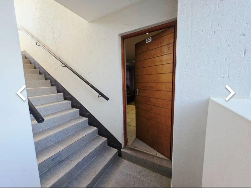 Entrance area featuring a timber front door and a concrete staircase with a metal handrail leading to the apartment unit.