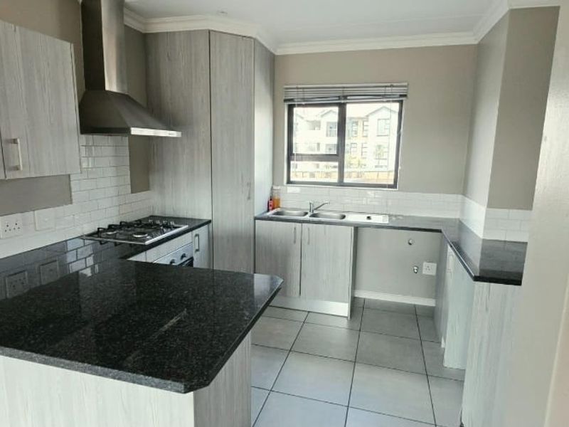 Modern kitchen featuring light wood-grain cabinetry, dark granite countertops, a gas hob with extractor fan, and a double sink with subway tile backsplash.