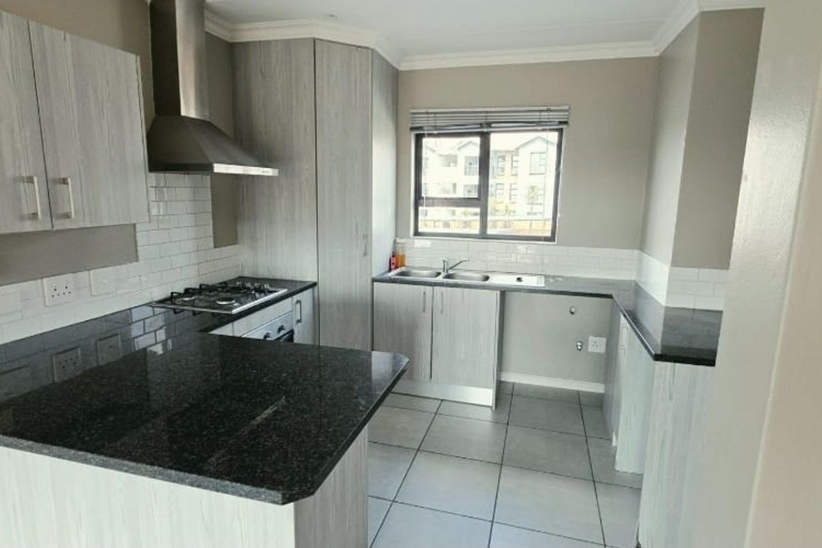 Modern kitchen featuring light wood-grain cabinetry, dark granite countertops, a gas hob with extractor fan, and a double sink with subway tile backsplash.