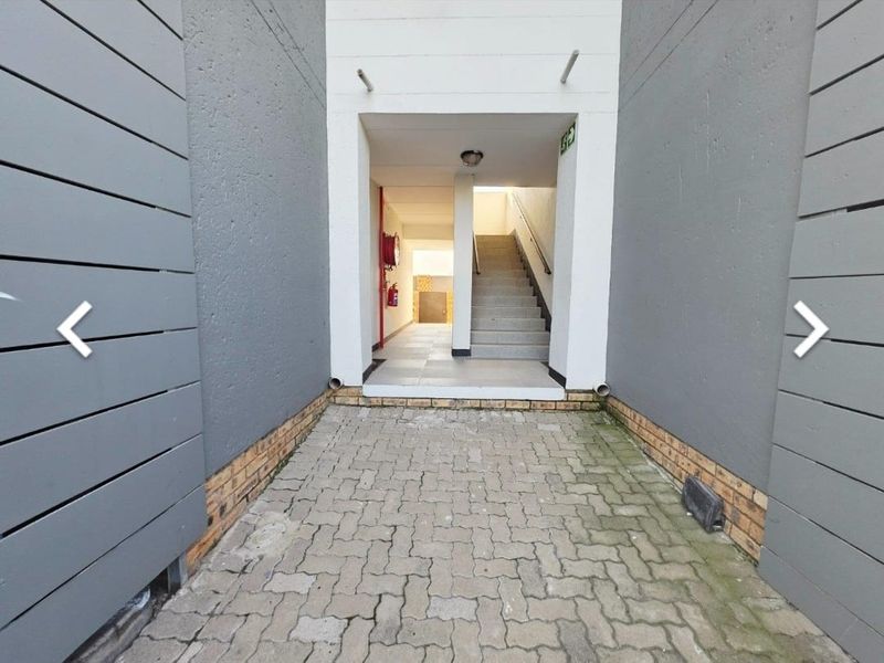 Exterior entrance area featuring a paved walkway leading to a staircase and building access point with fire safety equipment.