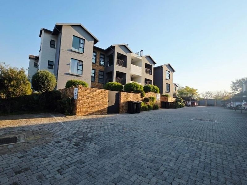 Exterior view of a multi-story apartment complex featuring a paved driveway, brick boundary walls, and residential balconies.
