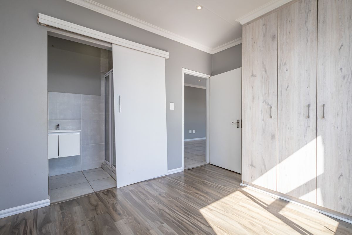 Spacious bedroom featuring modern laminate flooring, extensive built-in cupboards, and a convenient en-suite bathroom with a sliding door entry.