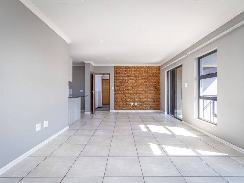 Spacious open-plan living area featuring neutral tiled flooring, an exposed brick feature wall, and large sliding doors leading to an outdoor space.