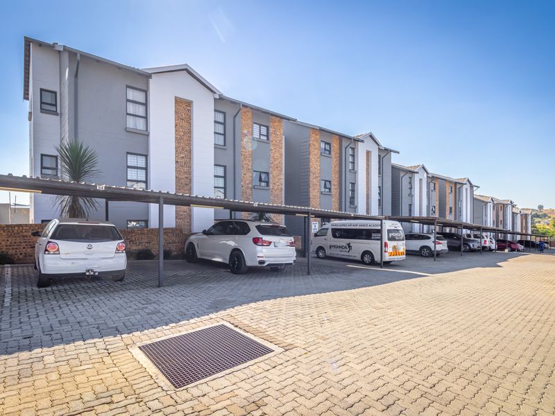 Exterior view of a modern apartment complex featuring a paved parking area with covered bays and well-maintained building facades.