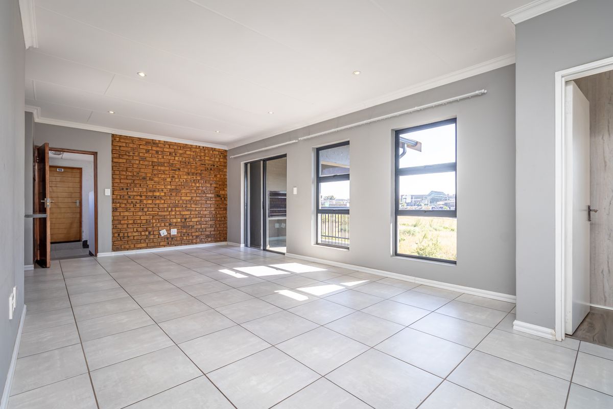 Spacious, light-filled living area featuring modern tiled floors, an exposed brick feature wall, and large aluminium windows with access to a balcony.