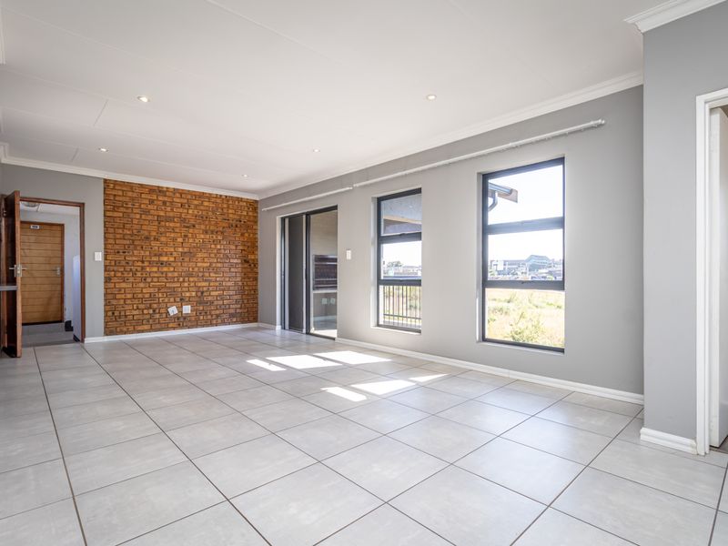 Spacious, light-filled living area featuring modern tiled floors, an exposed brick feature wall, and large aluminium windows with access to a balcony.
