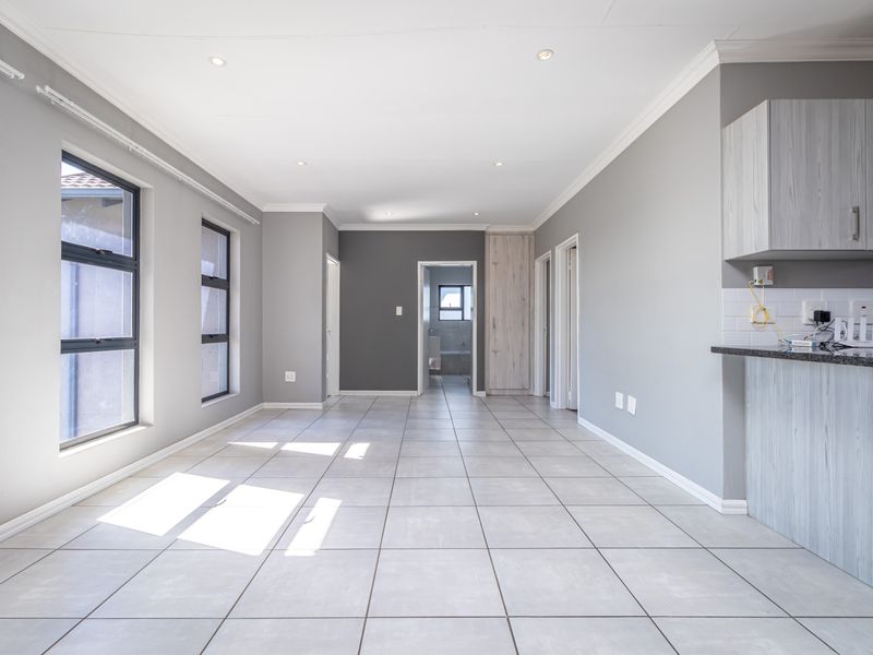Spacious open-plan living area featuring neutral grey walls, tiled flooring, recessed lighting, and a modern kitchen corner with granite countertops.