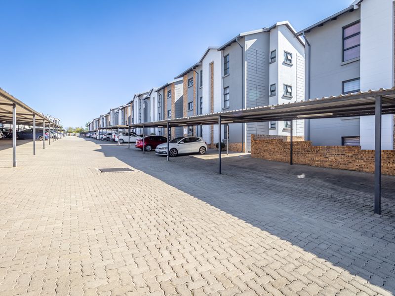 Exterior view of the apartment complex featuring paved parking area with covered bays and multi-story residential building facade.