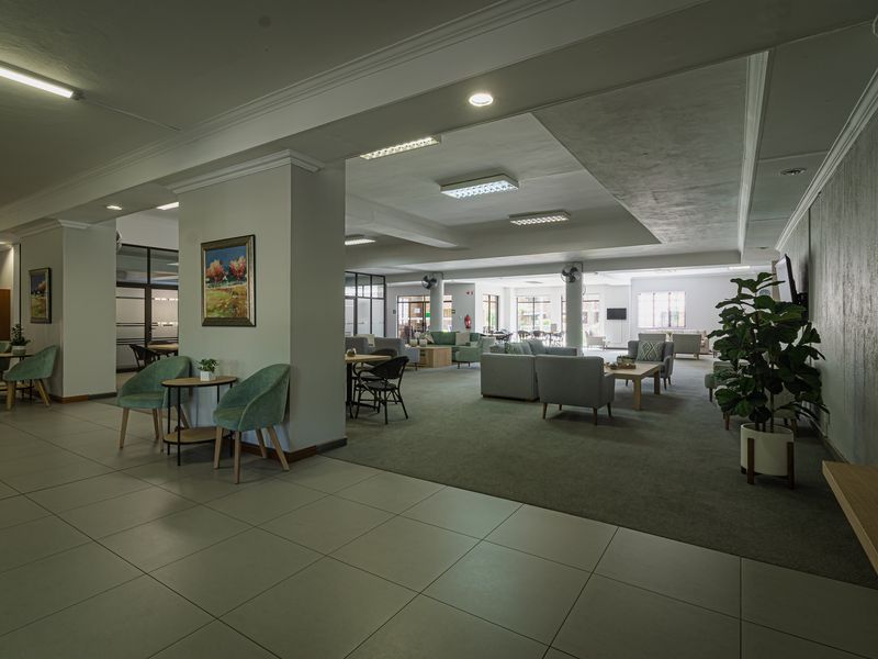 Spacious open-plan communal living area featuring a mix of tiled and carpeted flooring, recessed ceiling details, and structural columns in a well-maintained building.
