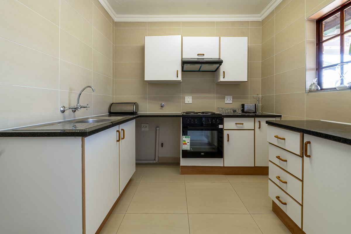 A functional kitchen featuring built-in cabinetry, granite countertops, a built-in oven with hob, and neutral wall and floor tiling.