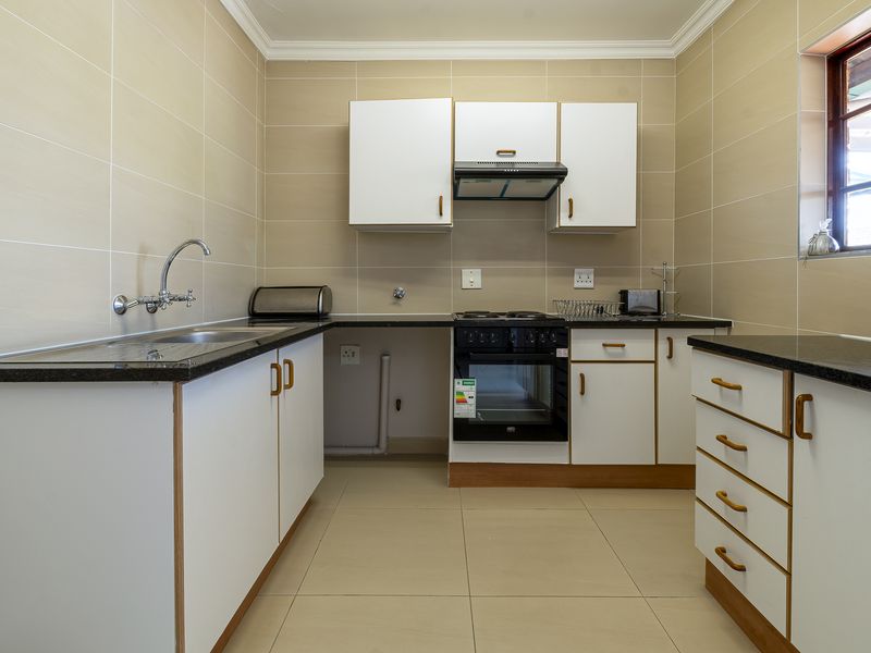 A functional kitchen featuring built-in cabinetry, granite countertops, a built-in oven with hob, and neutral wall and floor tiling.