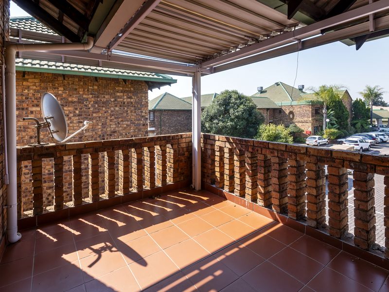 A covered balcony featuring brick balustrades and tiled flooring, offering an open outdoor space with views of the surrounding complex.