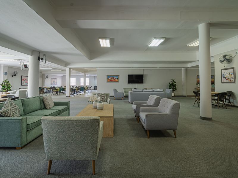Spacious open-plan living area featuring structural columns, carpeted flooring, and recessed ceiling lighting, suitable for versatile communal use.