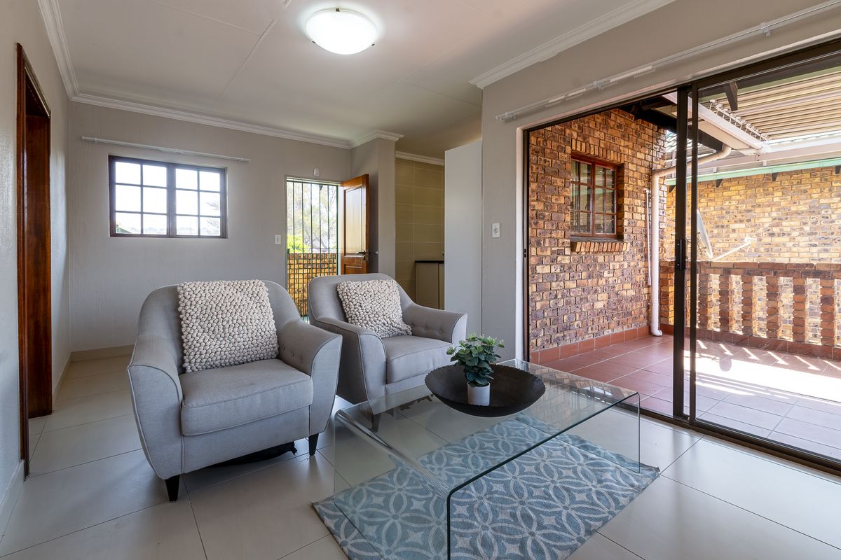 A bright living room featuring tiled floors, an exposed brick feature wall, and a sliding glass door providing access to an outdoor patio area.
