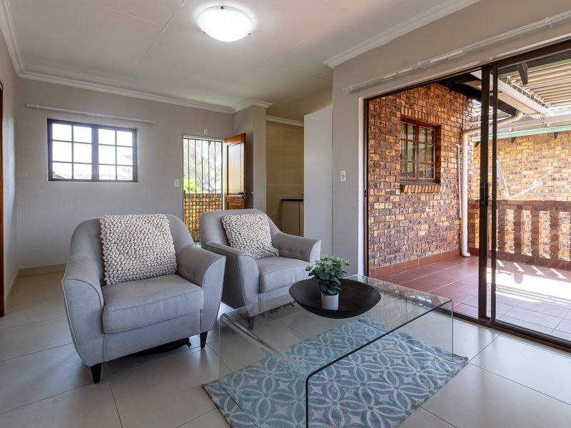 A bright living room featuring tiled floors, an exposed brick feature wall, and a sliding glass door providing access to an outdoor patio area.