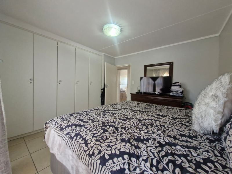 A bedroom featuring built-in cupboards, tiled flooring, and a ceiling light fixture, with an adjacent doorway leading to an en-suite bathroom.