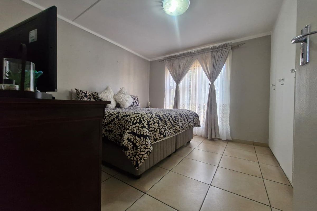 A functional bedroom featuring tiled flooring, built-in storage cupboards, and natural light through window curtains.
