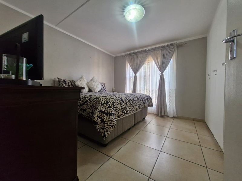 A functional bedroom featuring tiled flooring, built-in storage cupboards, and natural light through window curtains.
