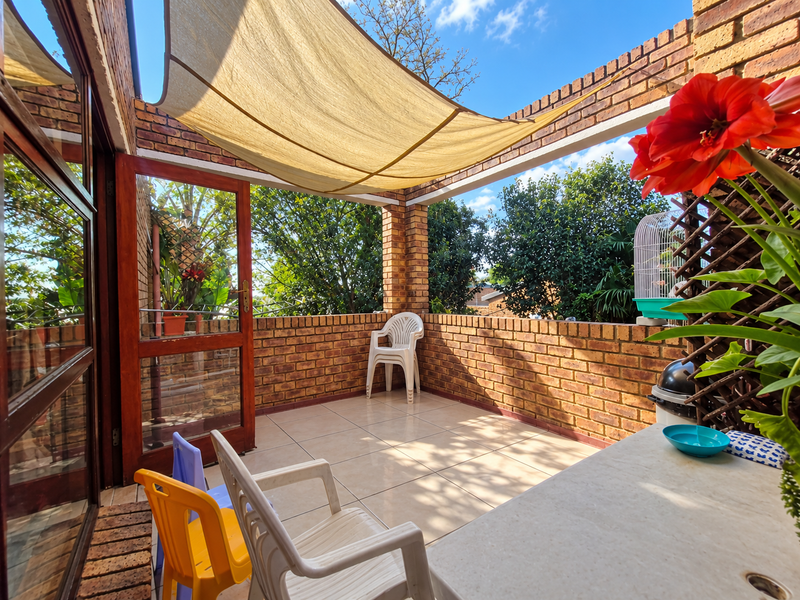 A private balcony featuring exposed brick walls, tiled flooring, and a shade sail, providing a comfortable outdoor space accessible through a timber-framed door.