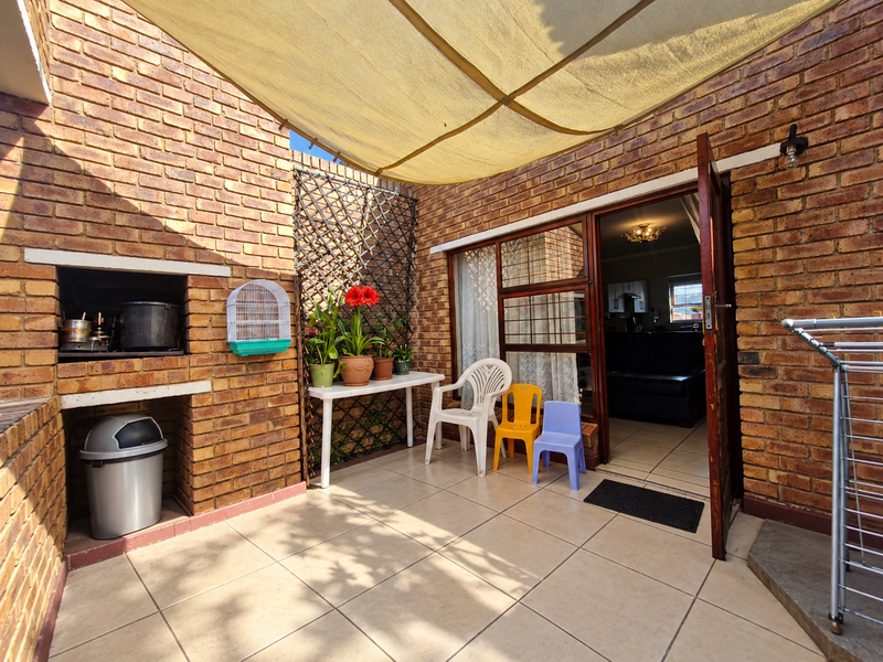 A private patio area featuring a built-in brick braai, tiled flooring, and a shade sail, providing a functional outdoor entertainment space.