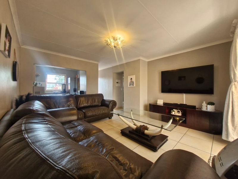 A comfortable living room featuring tiled flooring, neutral wall tones, and a coved ceiling, with an open-plan layout connecting to the kitchen area.