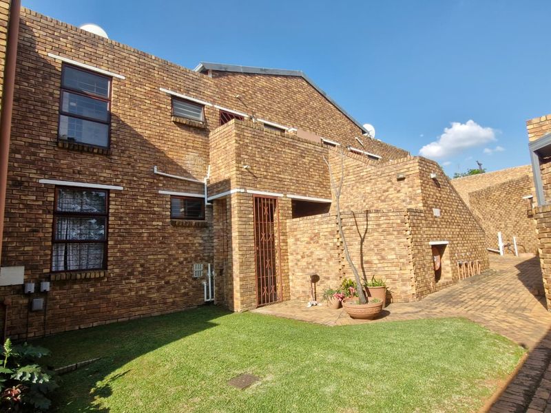 Rear view of a face brick apartment building featuring a private entrance, paved walkway, and a well-maintained lawn area.