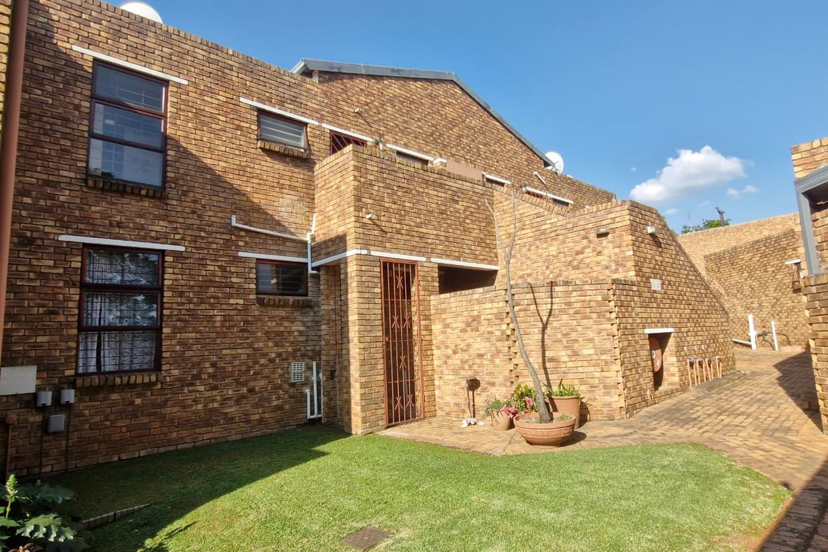 Rear view of a face brick apartment building featuring a private entrance, paved walkway, and a well-maintained lawn area.