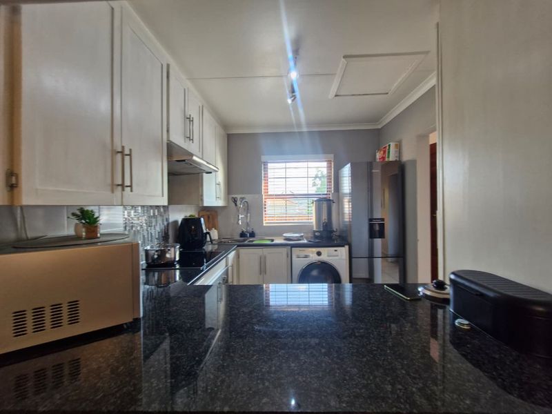 A functional kitchen featuring dark granite countertops, white cabinetry, and integrated appliances, offering a clean and practical workspace.