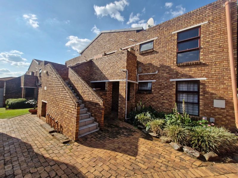 Rear exterior view of a face brick apartment building featuring a paved courtyard, external staircase, and established garden beds.