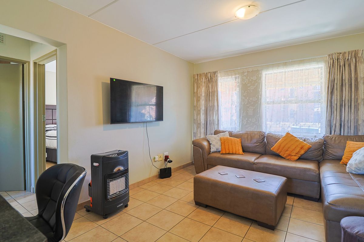 A functional living room featuring tiled flooring, neutral wall tones, and large windows allowing natural light, providing a comfortable space for relaxation.