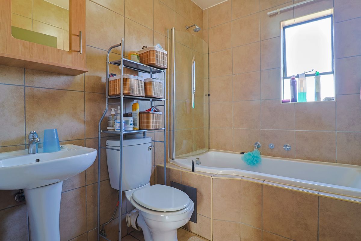 A functional bathroom featuring a pedestal basin, toilet, and a bathtub with a glass shower screen, finished with neutral wall tiling.