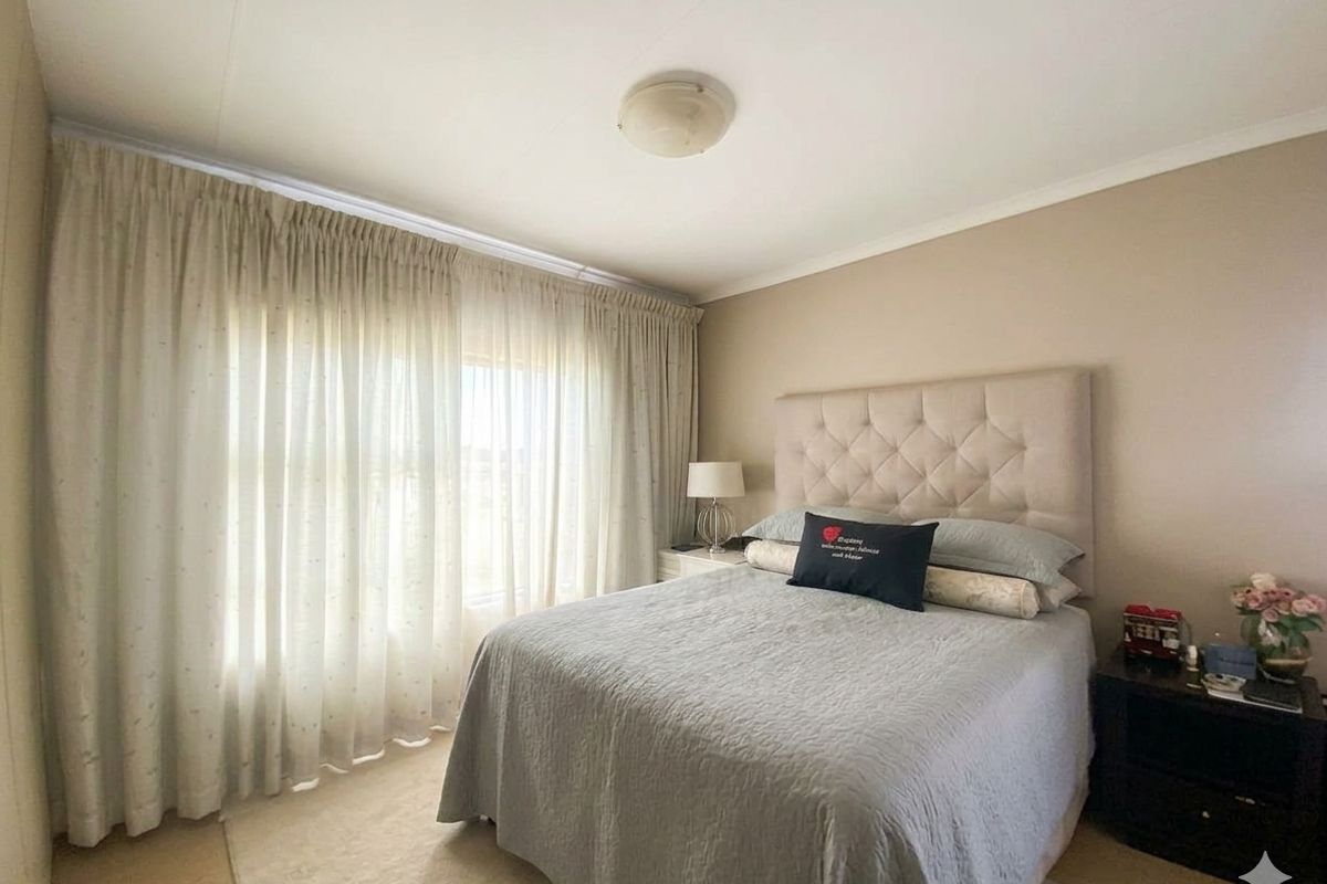 A well-maintained bedroom featuring neutral wall tones, carpeted flooring, and large windows dressed with floor-to-ceiling curtains.