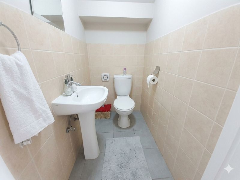 A compact guest bathroom featuring a pedestal basin, standard toilet, and neutral ceramic wall and floor tiling.