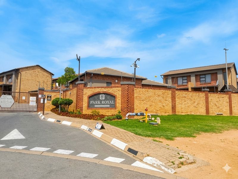 Front entrance view of Park Royal townhouse complex featuring brick boundary walls, security gate, and well-maintained paved access.