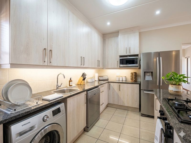 Modern kitchen featuring light wood-grain cabinetry, granite countertops, integrated appliances, and under-cabinet lighting with tiled flooring.