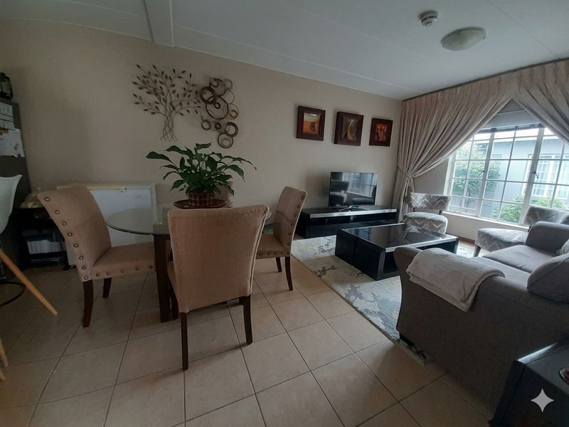Open-plan living and dining area featuring neutral tiled flooring, large windows with curtains, and a functional layout suitable for comfortable daily living.
