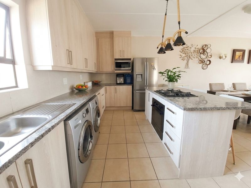 Modern open-plan kitchen featuring light wood cabinetry, granite countertops, a central island with a gas hob, and integrated appliances.