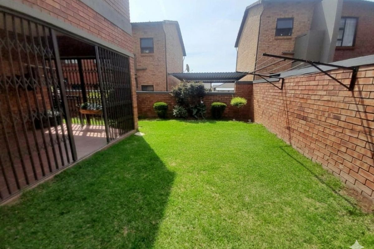 A private rear garden featuring a well-maintained lawn, brick boundary walls, and a covered patio area with security gates.