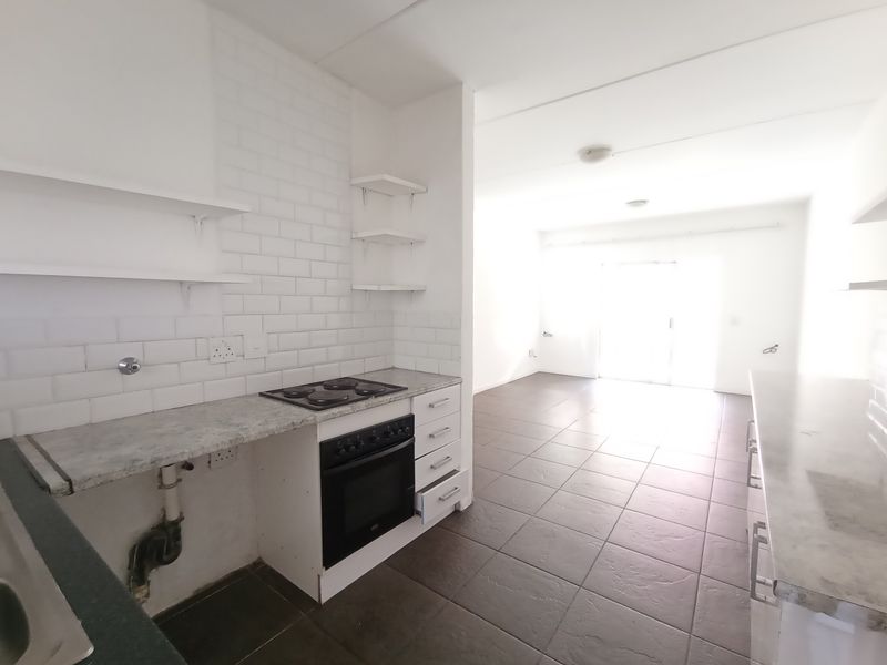 An open-plan kitchen and living area featuring tiled floors, subway tile backsplash, built-in oven, and hob, with a bright, neutral aesthetic.