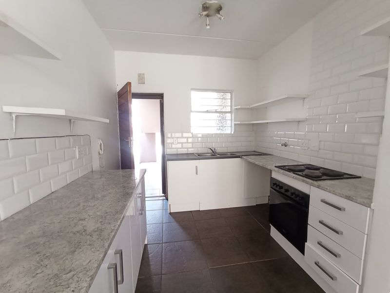 A clean, functional kitchen featuring white cabinetry, subway tile backsplash, stone-look laminate countertops, built-in oven, and electric hob with direct access to an outdoor area.