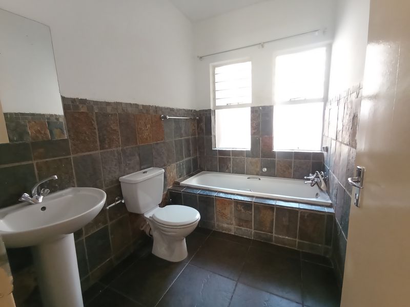 A functional bathroom featuring a pedestal basin, toilet, and a built-in bathtub with natural stone-style wall tiling and dark floor tiles.