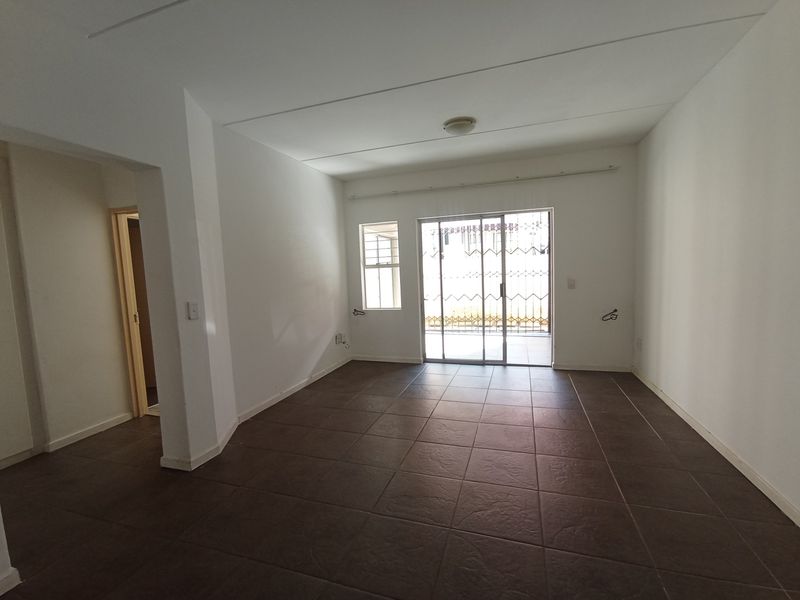 A bright, empty living area featuring dark tiled flooring and a sliding glass door that provides access to an outdoor space.