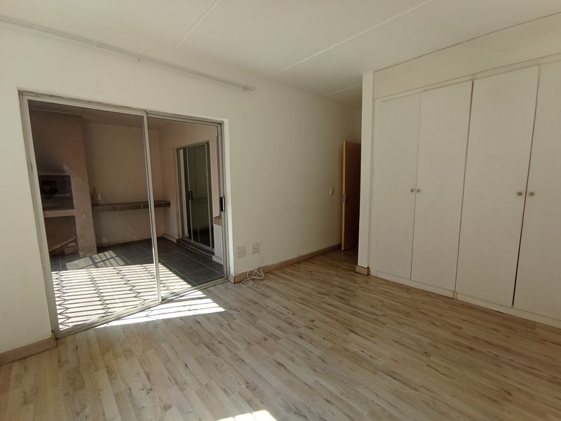 Empty bedroom featuring light laminate flooring, built-in cupboards, and a sliding glass door providing access to an outdoor patio area.