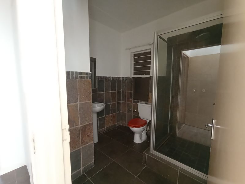 A functional bathroom featuring a pedestal basin, toilet, and a glass-enclosed shower with dark tiled finishes.