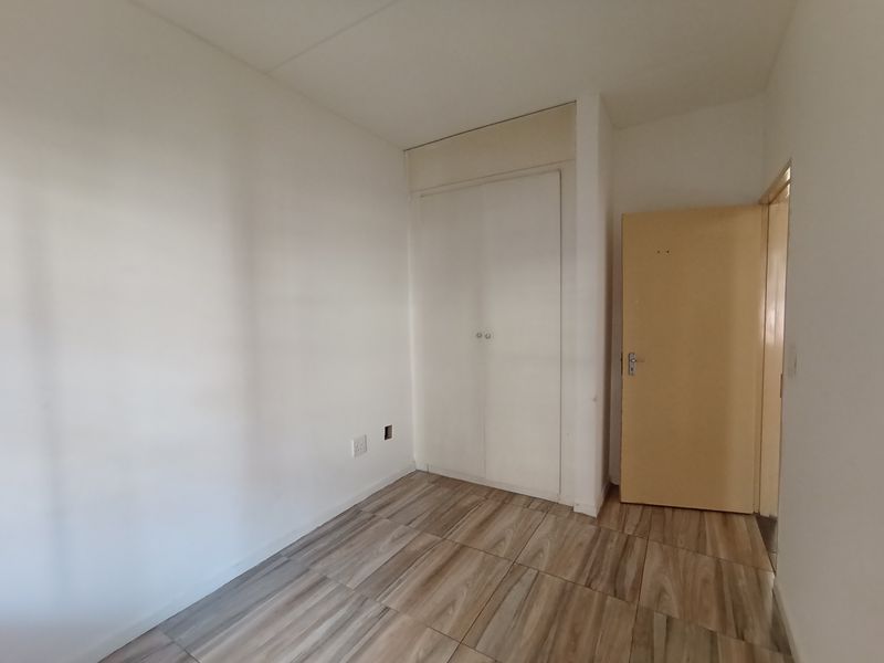 An empty bedroom featuring wood-look tile flooring and a built-in wardrobe, offering a clean, neutral space ready for personalization.