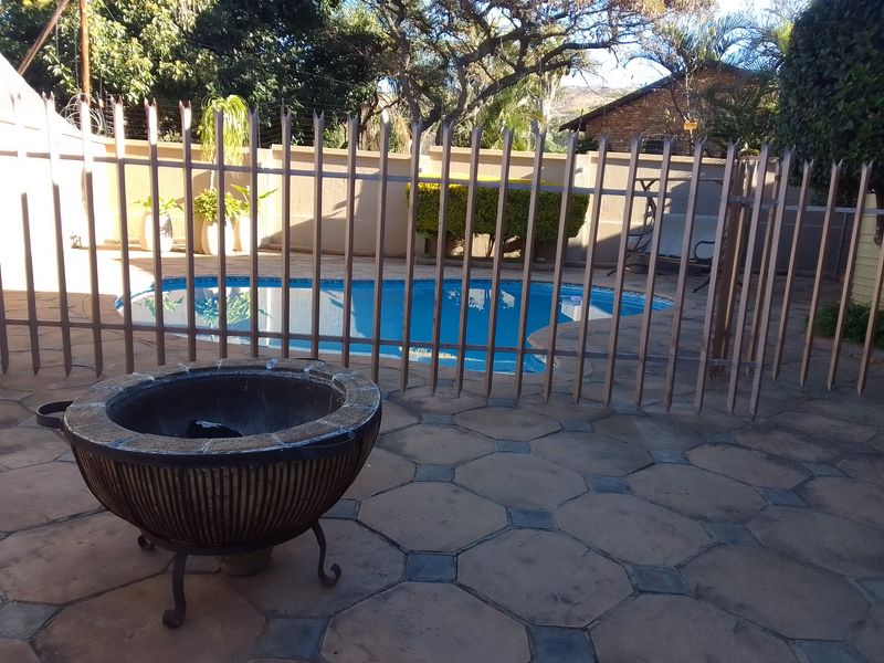 Outdoor patio area featuring a swimming pool enclosed by a metal security fence and paved flooring.