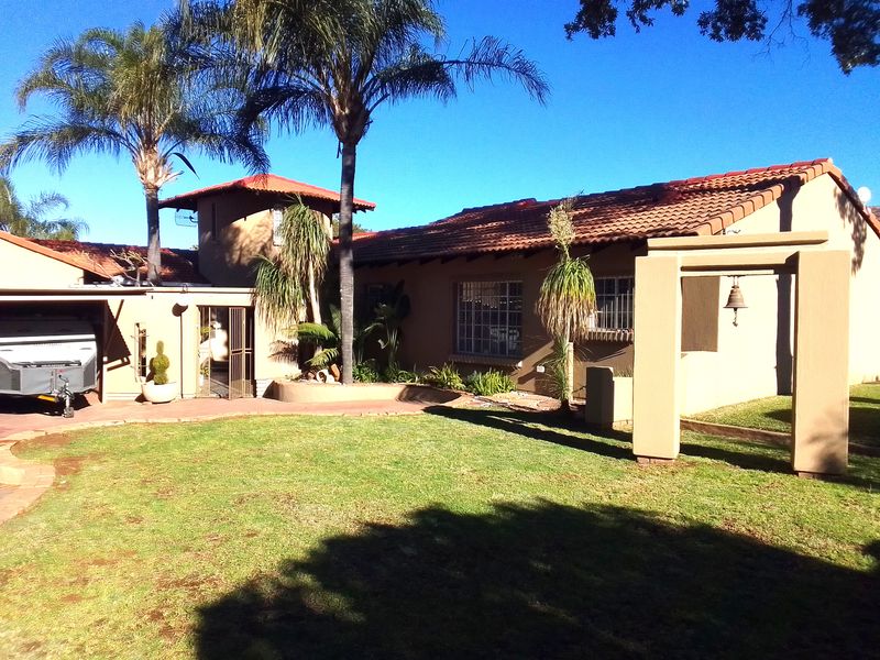 A well-maintained rear exterior view featuring a terracotta tiled roof, paved patio area, and a spacious garden with established trees.