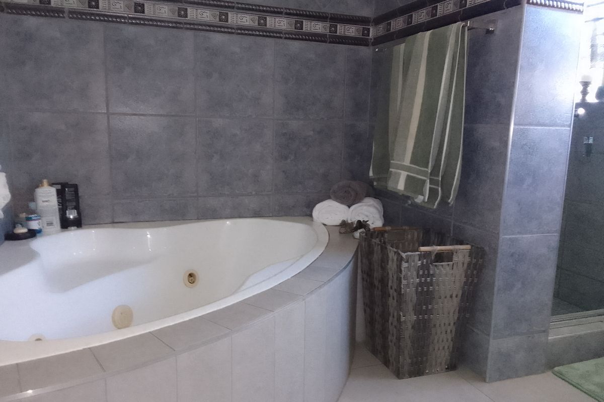 A bathroom featuring a corner spa bath with grey tiled walls and a separate shower enclosure.