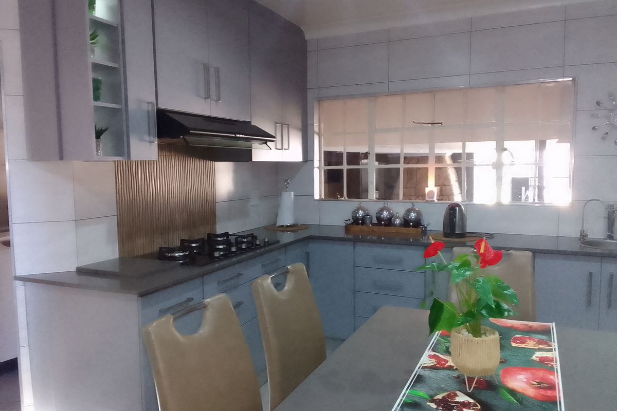 Modern kitchen featuring grey built-in cabinetry, stone countertops, a gas hob with extractor fan, and a tiled backsplash with a pass-through window.