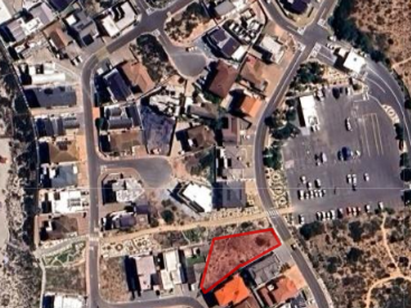 Aerial view of a vacant residential land plot situated in a coastal neighborhood, highlighting the property boundaries and surrounding infrastructure.
